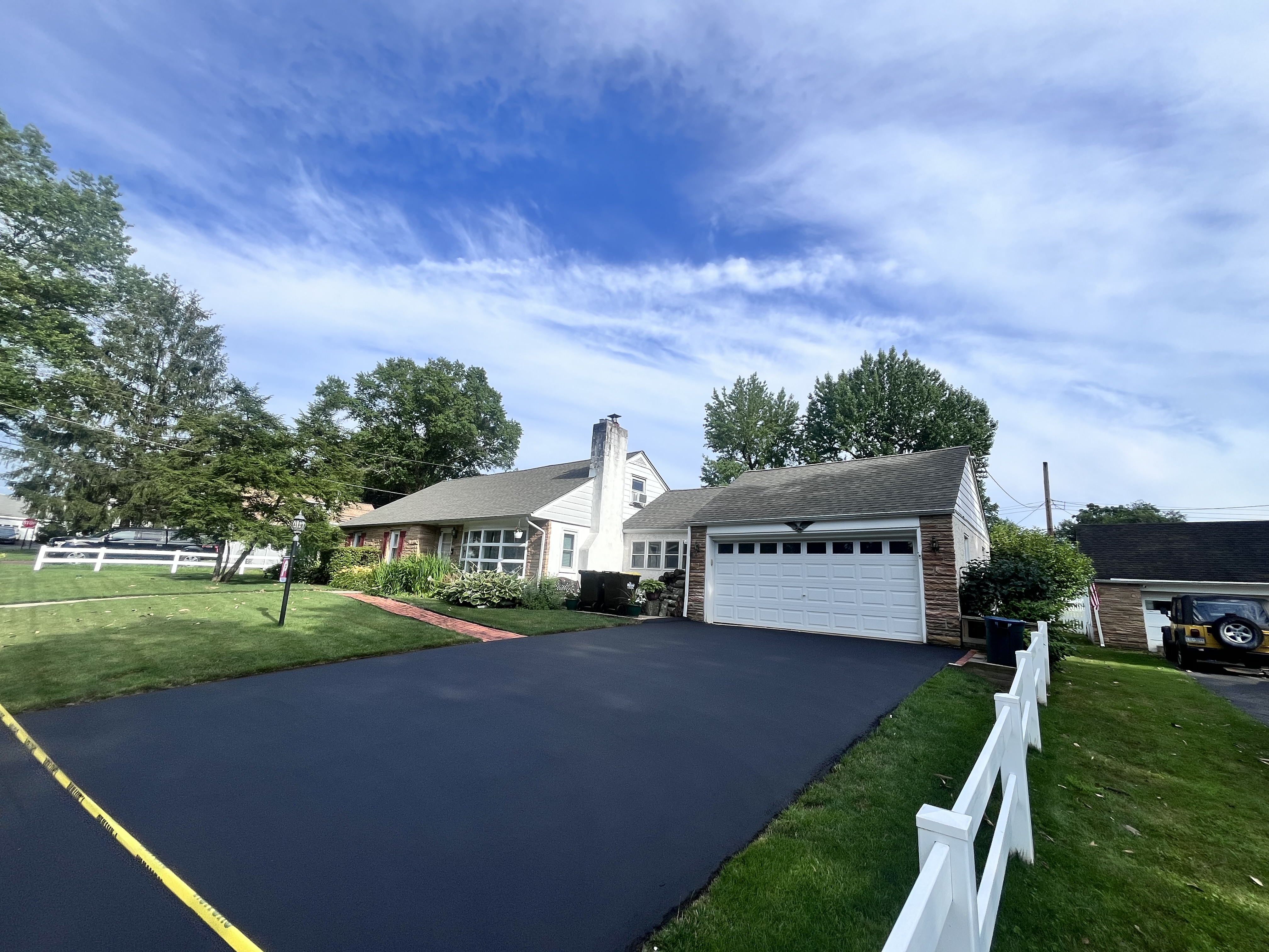 Ranch home driveway sealcoating — clean finish along white fence