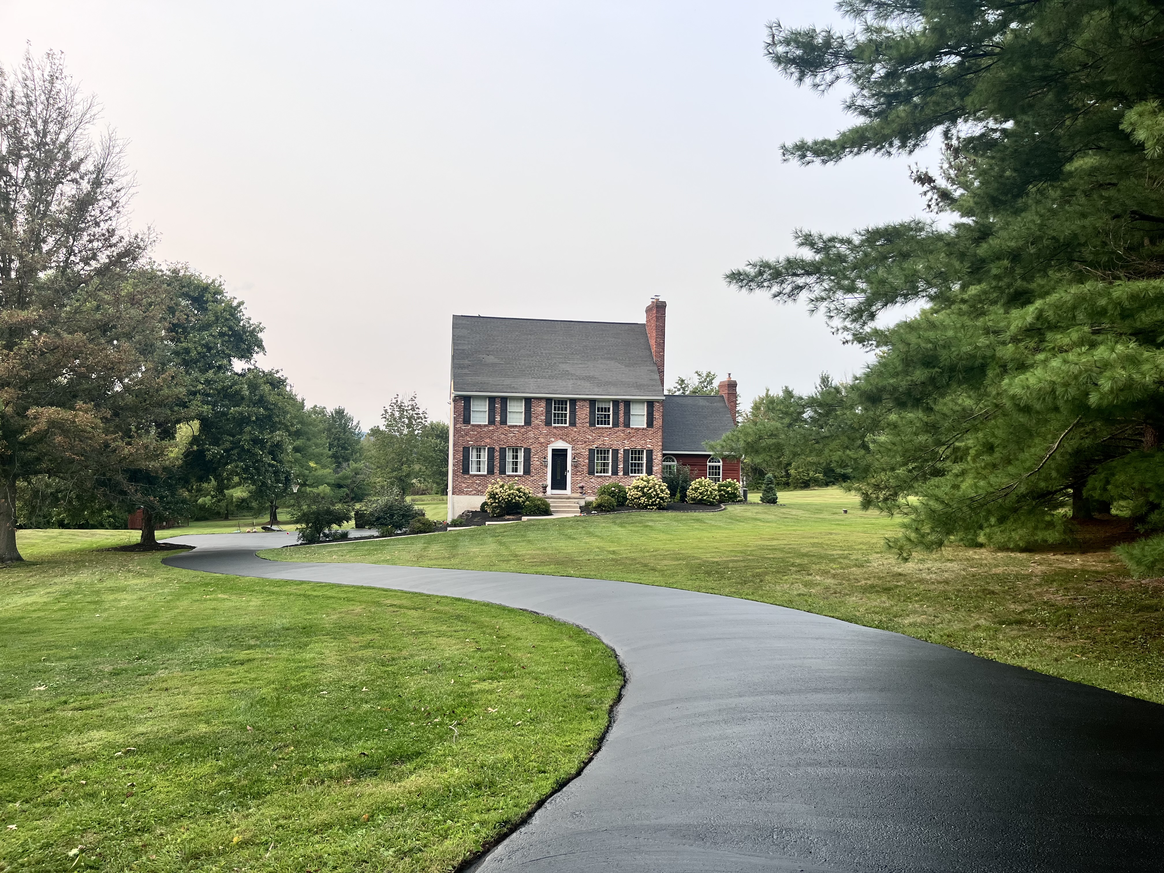 Long winding colonial driveway freshly sealed — residential sealcoating project